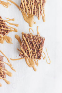 A stack of no bake peanut butter and chocolate marshmallow treats with a peanut butter drizzle