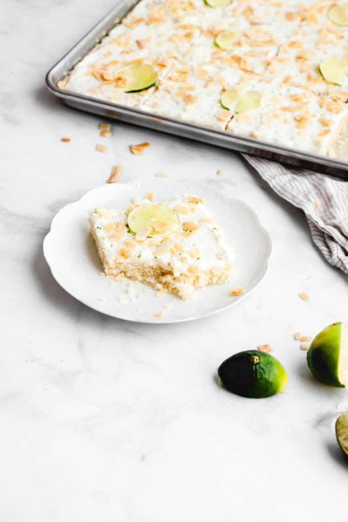 A piece of lime and coconut sheet cake on a plate with a bit taken out of it.
