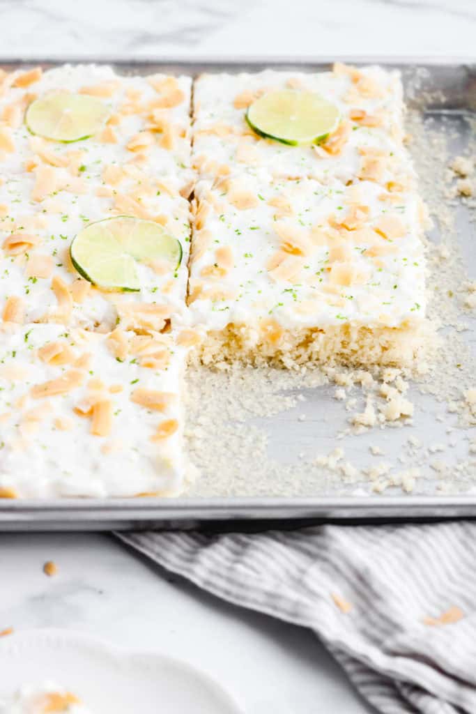 Coconut and lime sheet cake in a pan with some slices taken out.