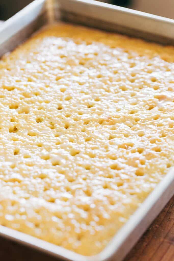A process shot of lime cake in a sheet pan with holes to soak up the coconut.