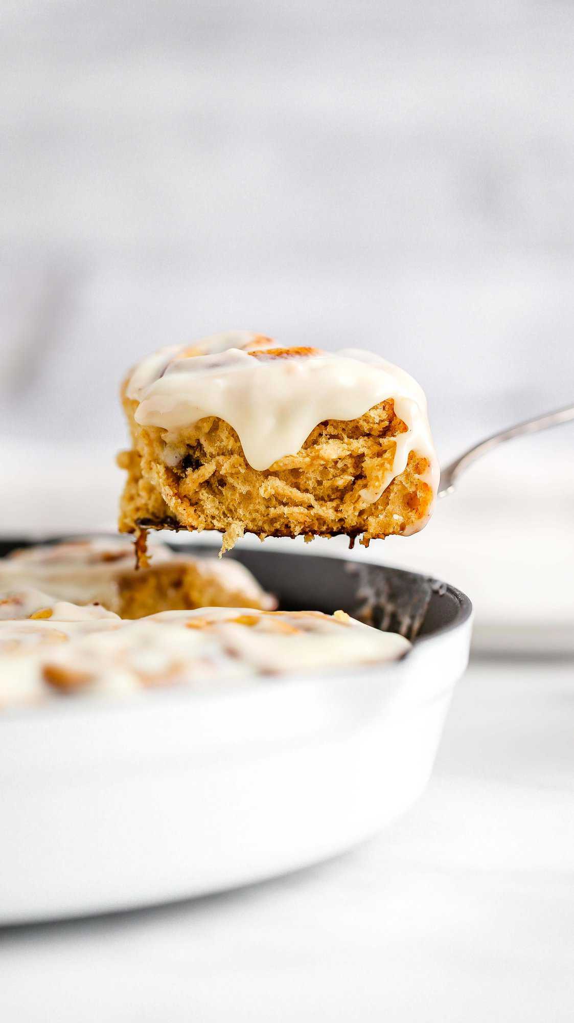 a pumpkin cinnamon roll lifted out of a cast iron skillet