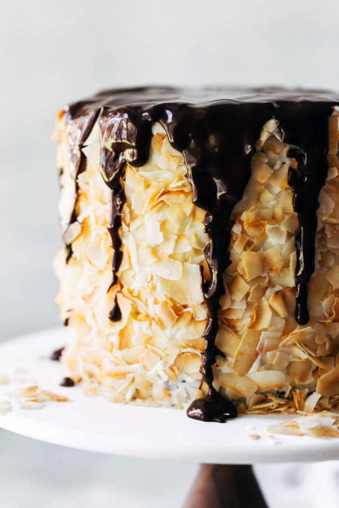 a layer cake covered in coconut with chocolate dripping down the sides