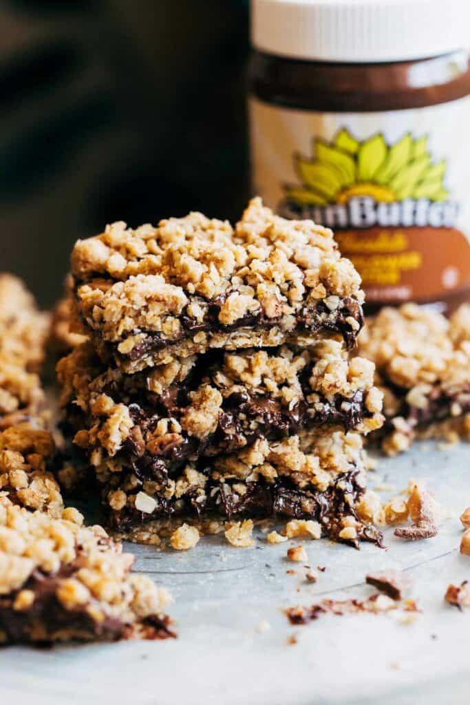 a stack of chocolate crumble bars with a jar of sunbutter