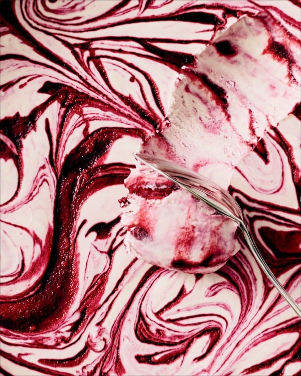 A spoon lifting red velvet ice cream from a pink and red swirl.
