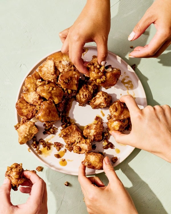 Hands sharing sticky maple pecan monkey bread from a plate.