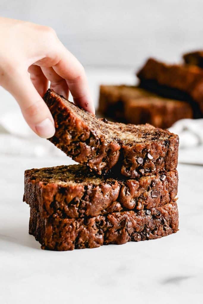 lifting a slice of banana bread from a stack of slices