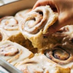 lifting a cinnamon roll out of a baking pan