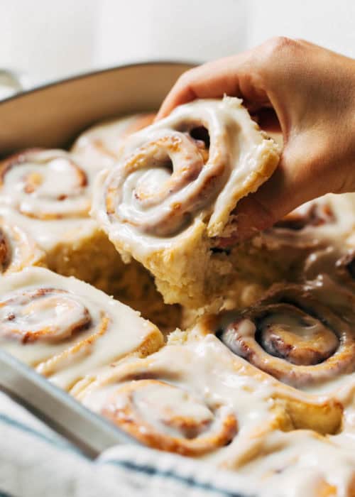 lifting a cinnamon roll out of a baking pan