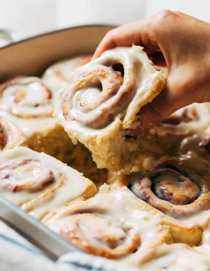 lifting a cinnamon roll out of a baking pan