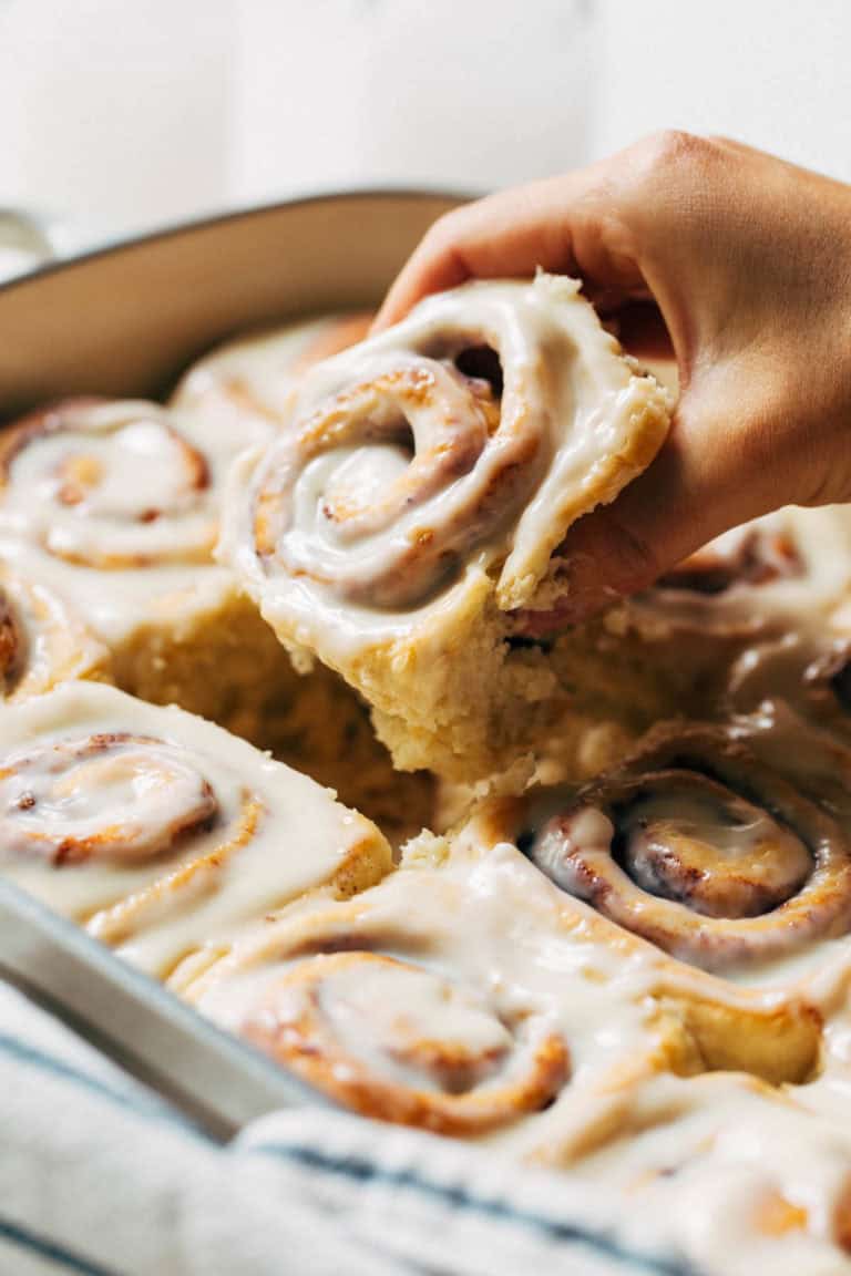 lifting a cinnamon roll out of a baking pan