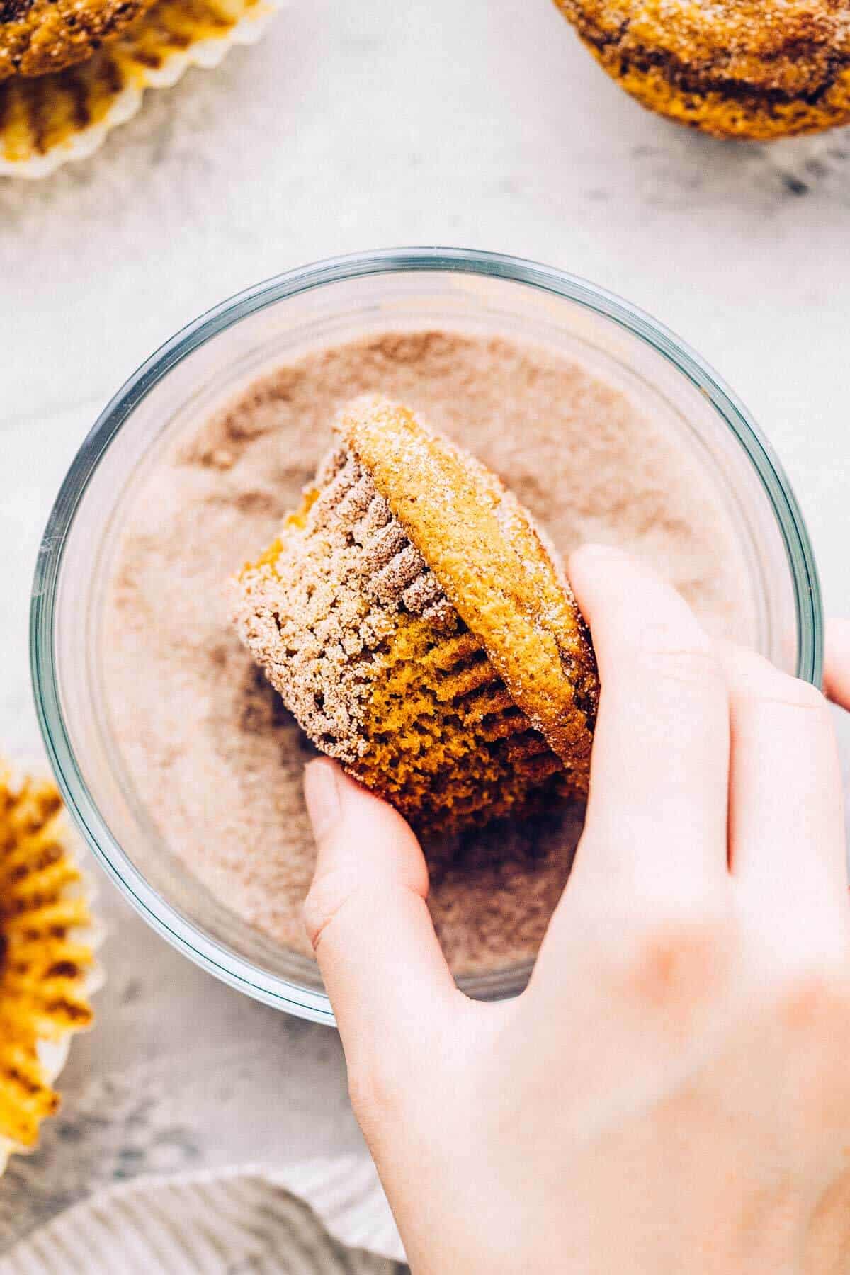 tossing a pumpkin muffin in a bowl of cinnamon and sugar to coat