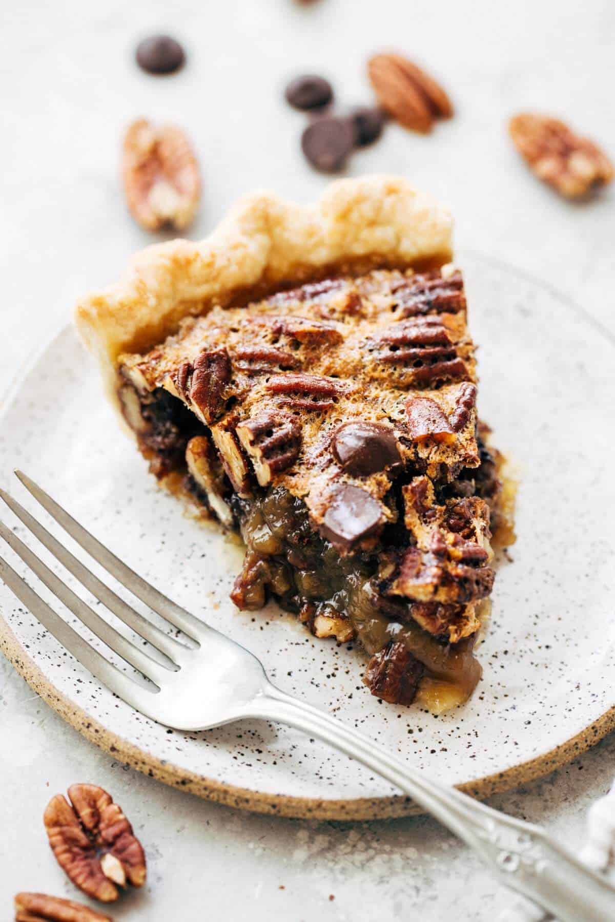 Slice of chocolate pecan pie with a fork on a white plate.