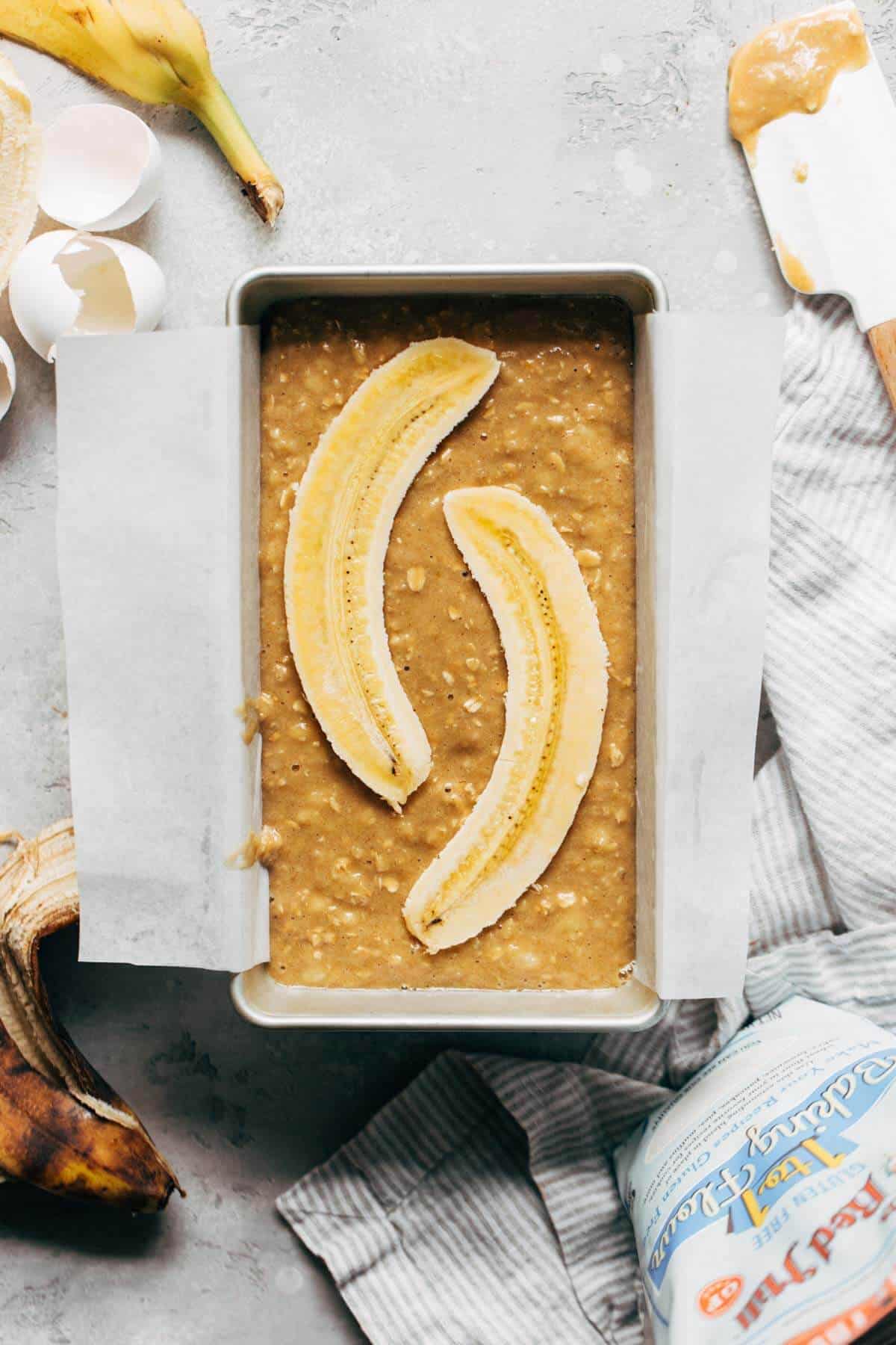 banana bread batter in a loaf pan topped with a lengthways sliced banana