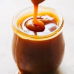 a jar of homemade salted caramel with a spoon drizzling caramel into it