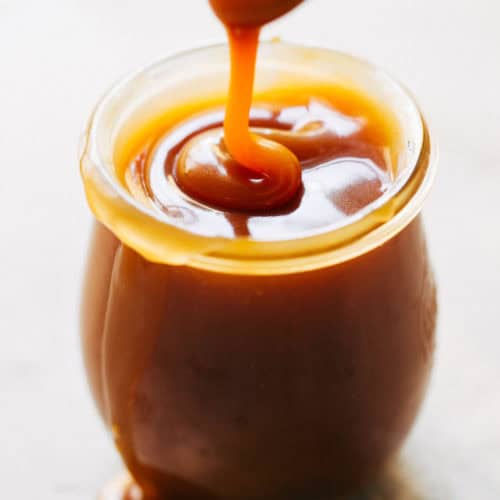 a jar of homemade salted caramel with a spoon drizzling caramel into it