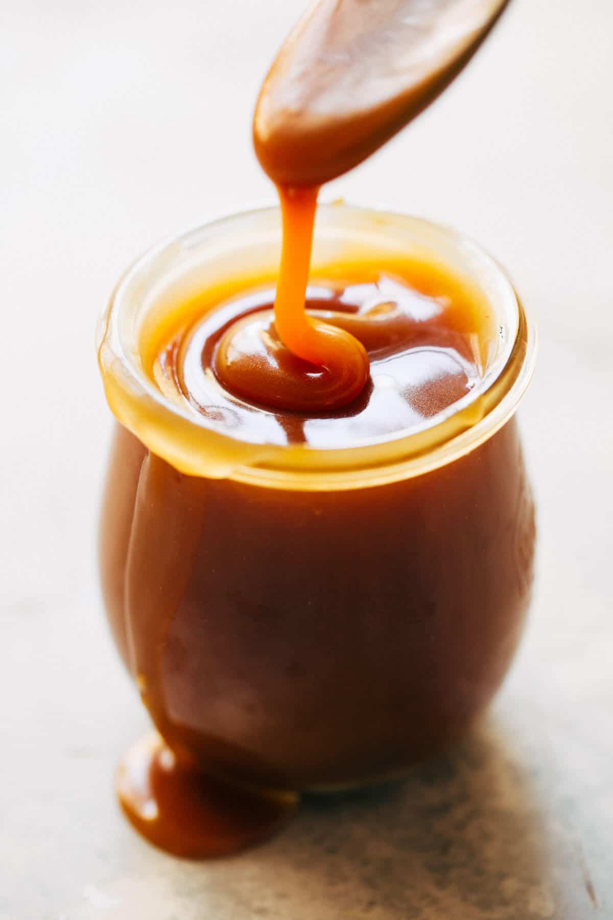 a jar of homemade salted caramel with a spoon drizzling caramel into it