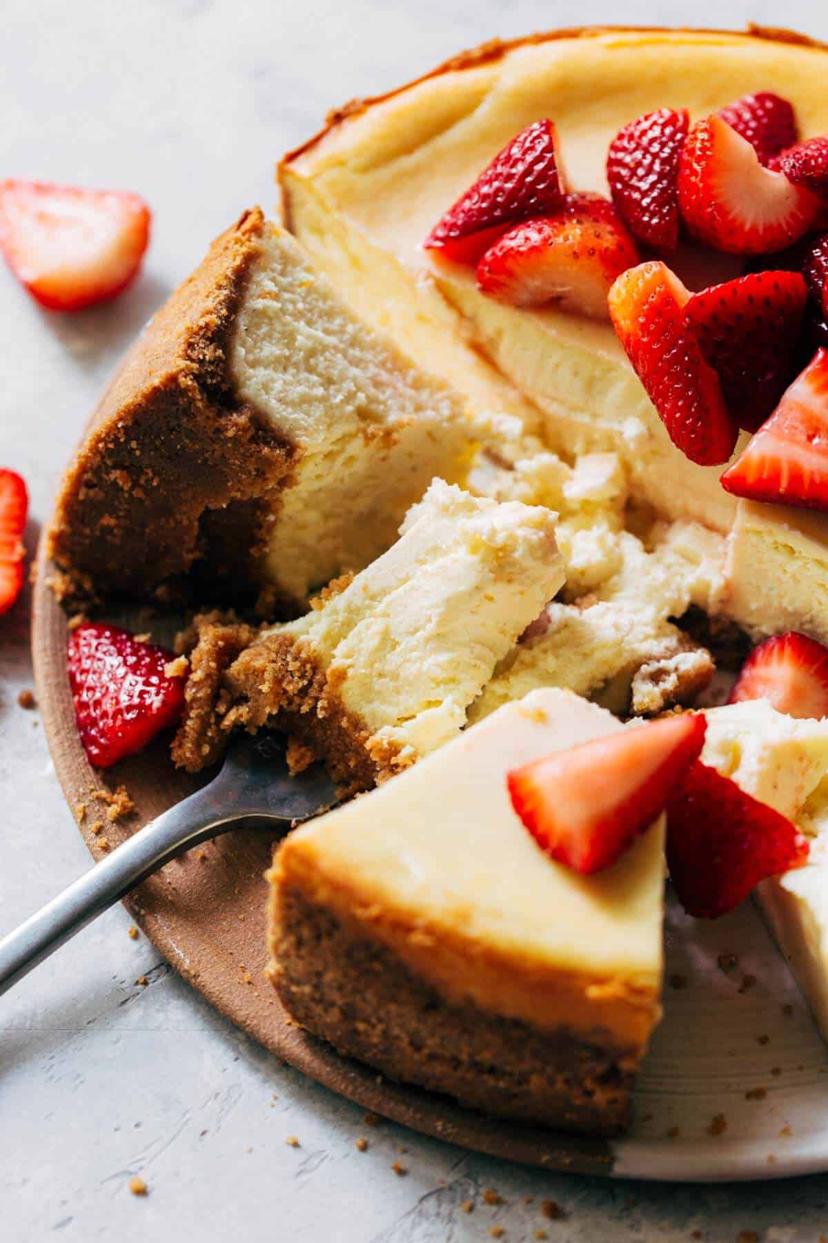 a fork dug into a whole cheesecake topped with fresh strawberries 