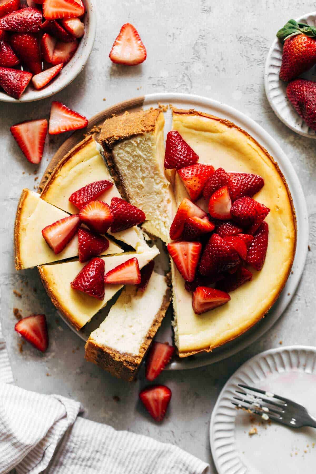a whole cheesecake sliced into topped with macerated strawberries