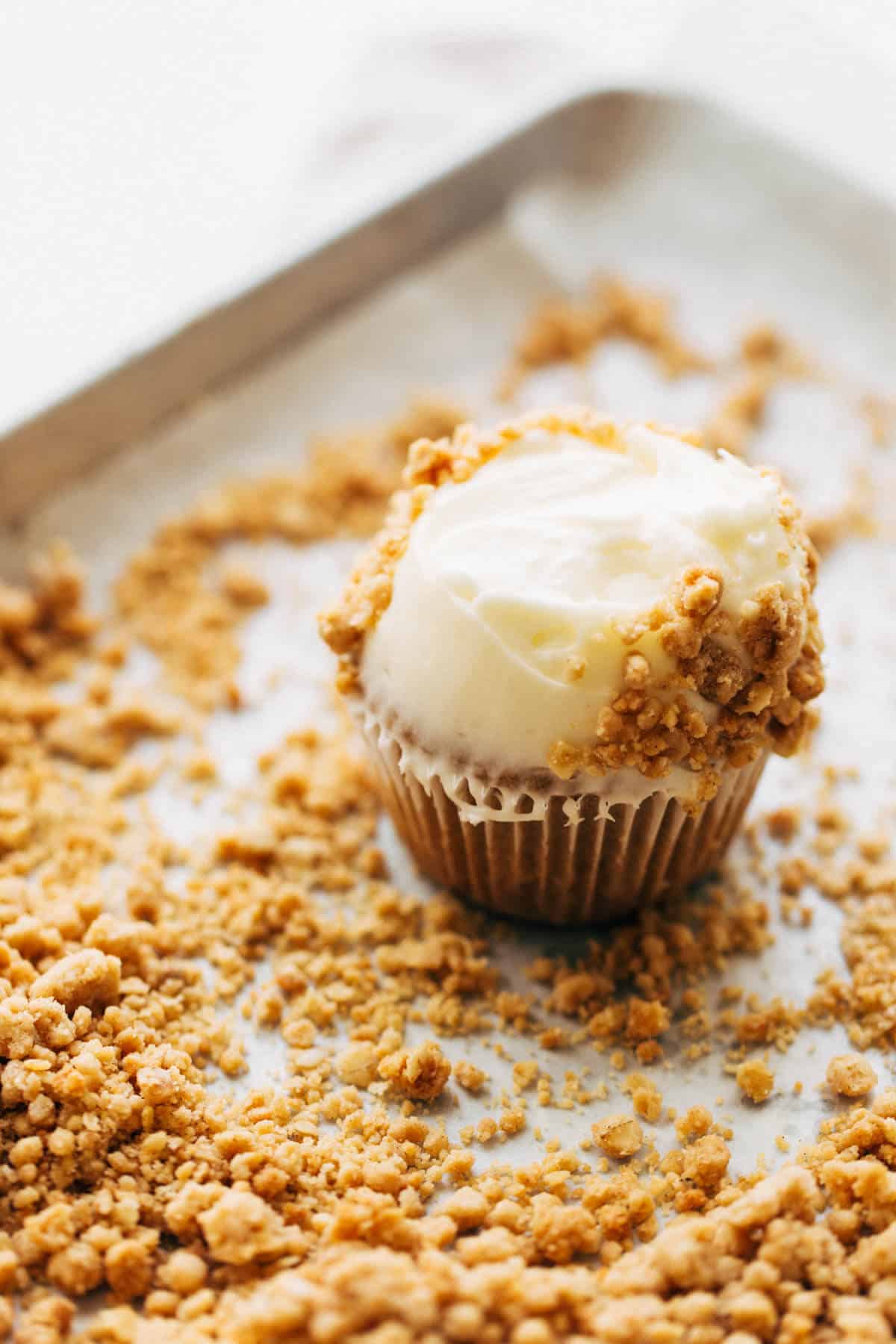 a cupcake on a tray of oat crumble with the frosting half coated in crumble