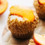 close up on a cupcake topped with a fresh peach slice