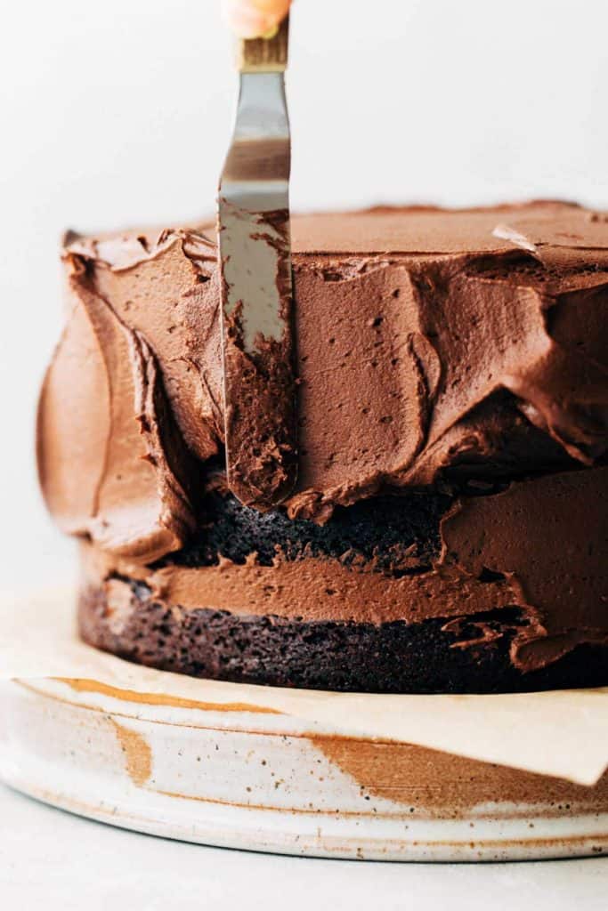 spreading chocolate frosting onto a layered chocolate cake