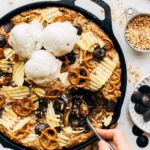 digging a spoon into a giant skillet cookie filled with pretzels, potato chips, and chocolate
