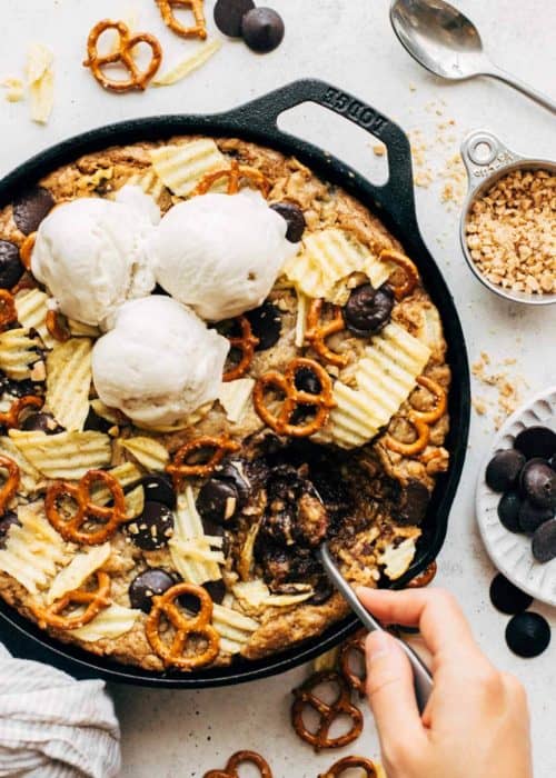 digging a spoon into a giant skillet cookie filled with pretzels, potato chips, and chocolate