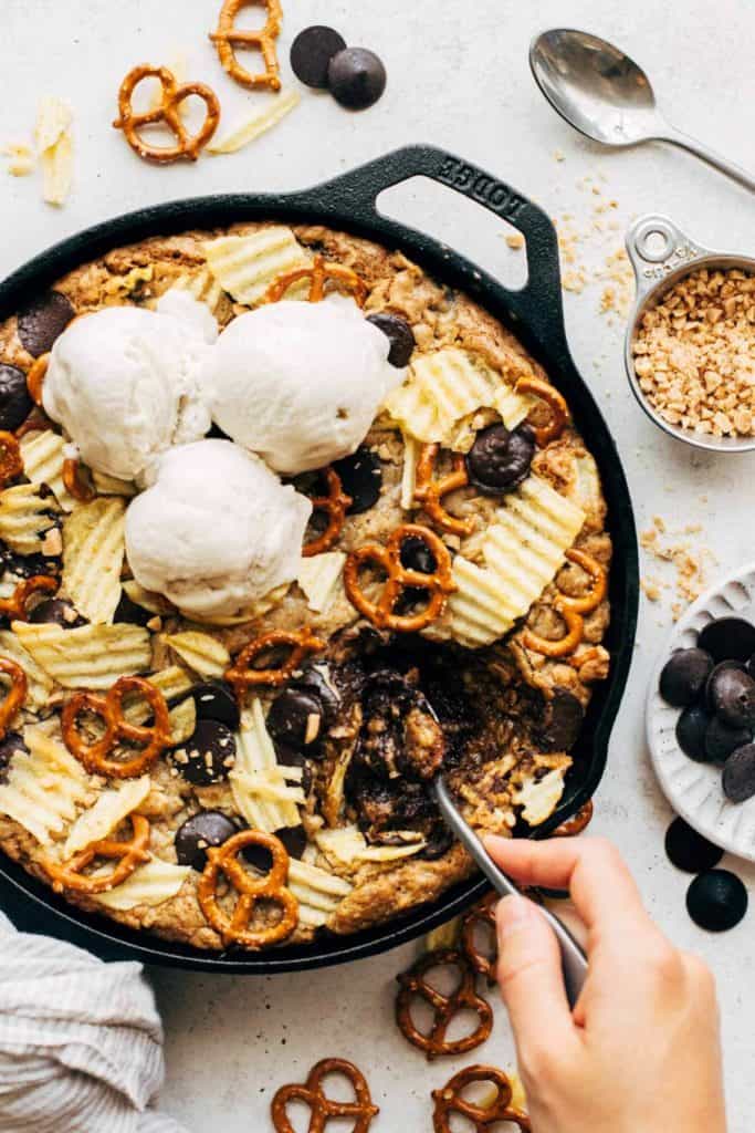 digging a spoon into a giant skillet cookie filled with pretzels, potato chips, and chocolate