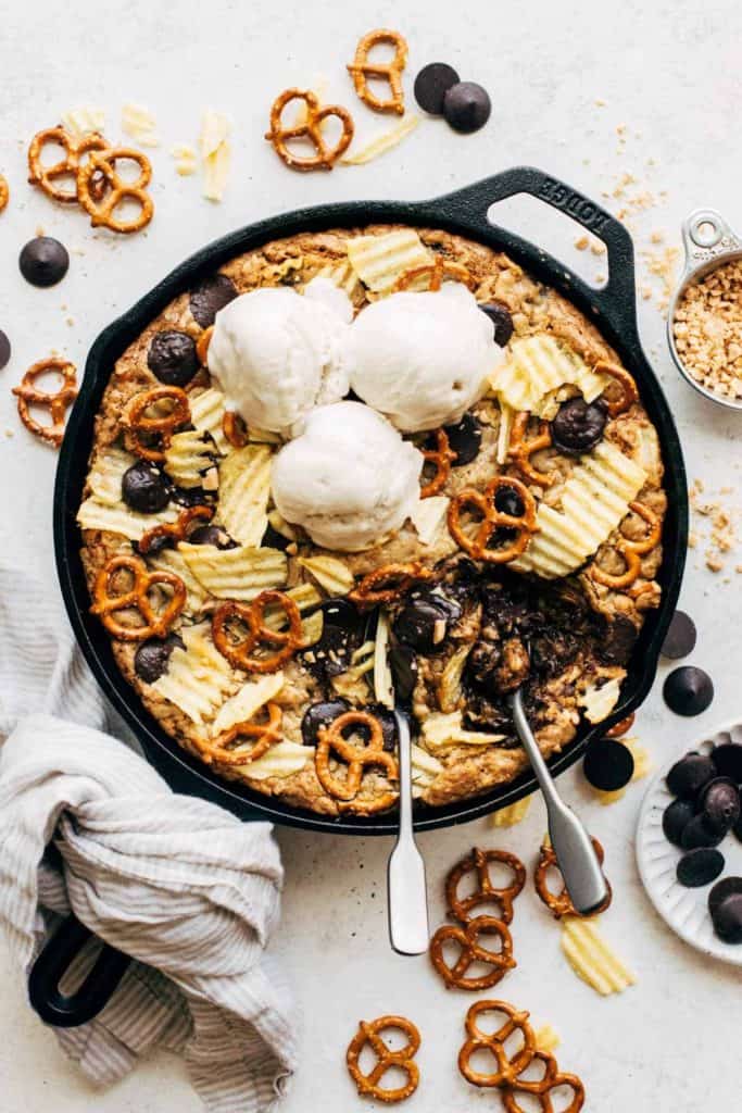 an overhead view of a compost skillet cookie with potato chips, pretzels, chocolate, and ice cream on top