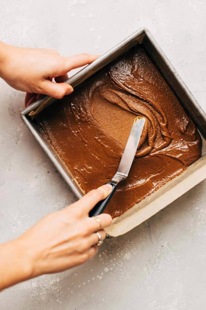 spreading gingerbread brownie batter into the bottom of a square baking dish