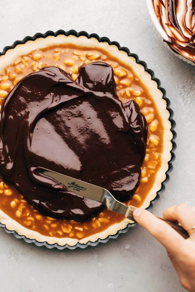 spreading chocolate on top of a layer of peanut caramel