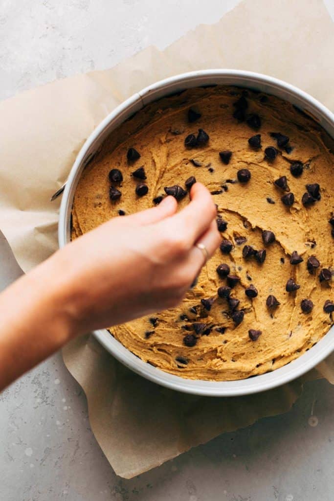 sprinkling chocolate chips on top of pumpkin cookie cake dough
