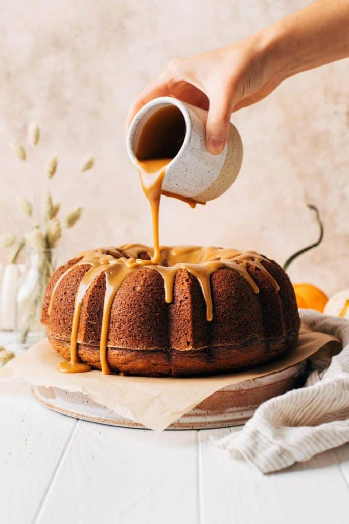 pouring butterscotch sauce on top of a pumpkin bundt cake