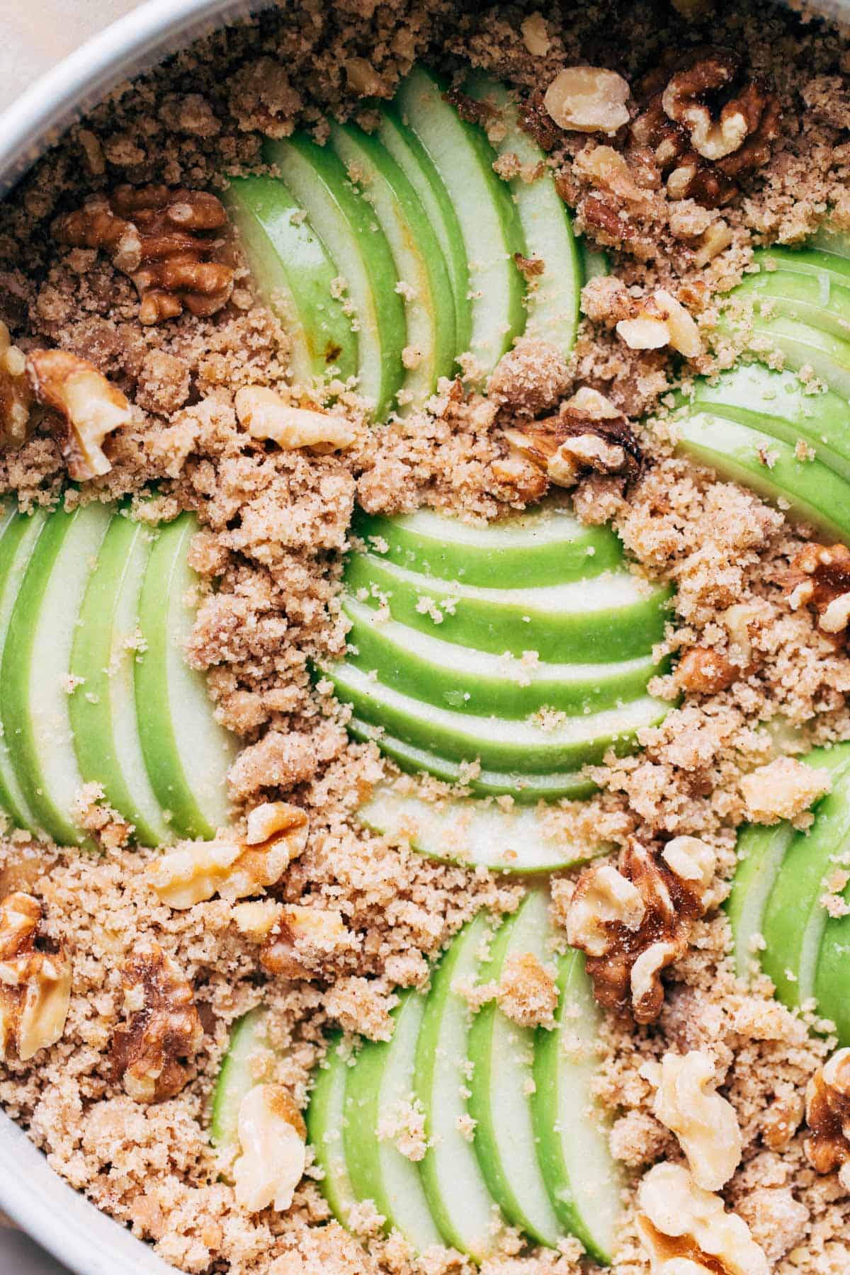 close up on the top of an apple cake topped with apple slices and crumble topping, before it's baked