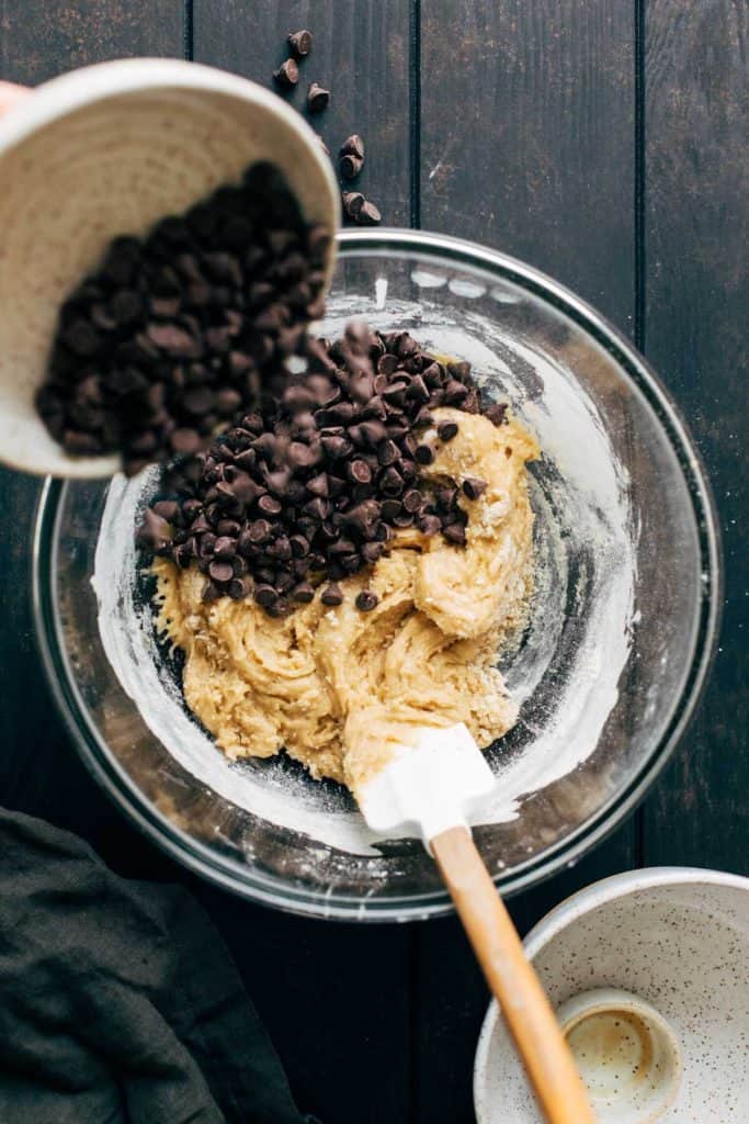 pouring chocolate chips into a bowl of cookie dough