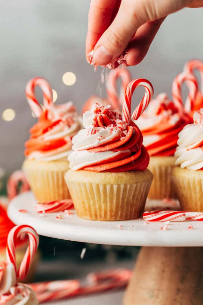 sprinkling crushed candy canes on top of a peppermint cupcake