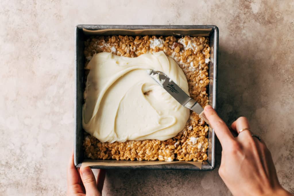 spreading white chocolate ganache on top of no bake cookie butter marshmallow treats