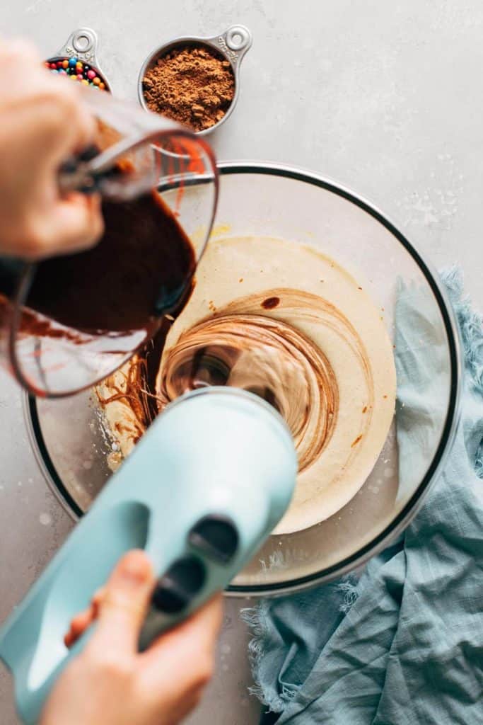 pouring melted chocolate into a bowl of whipped eggs and sugar