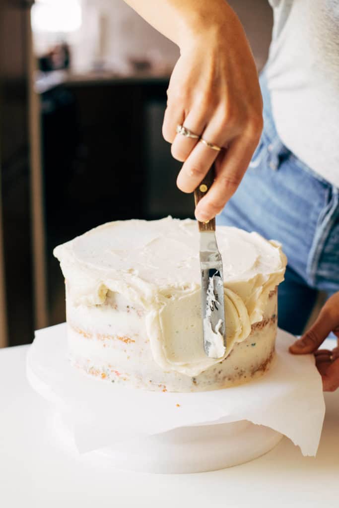 spreading buttercream on the sides of a cake
