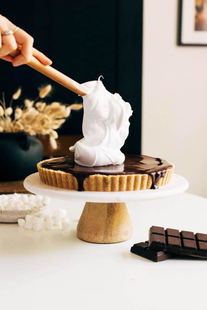 scooping marshmallow meringue on top of a smores cheesecake