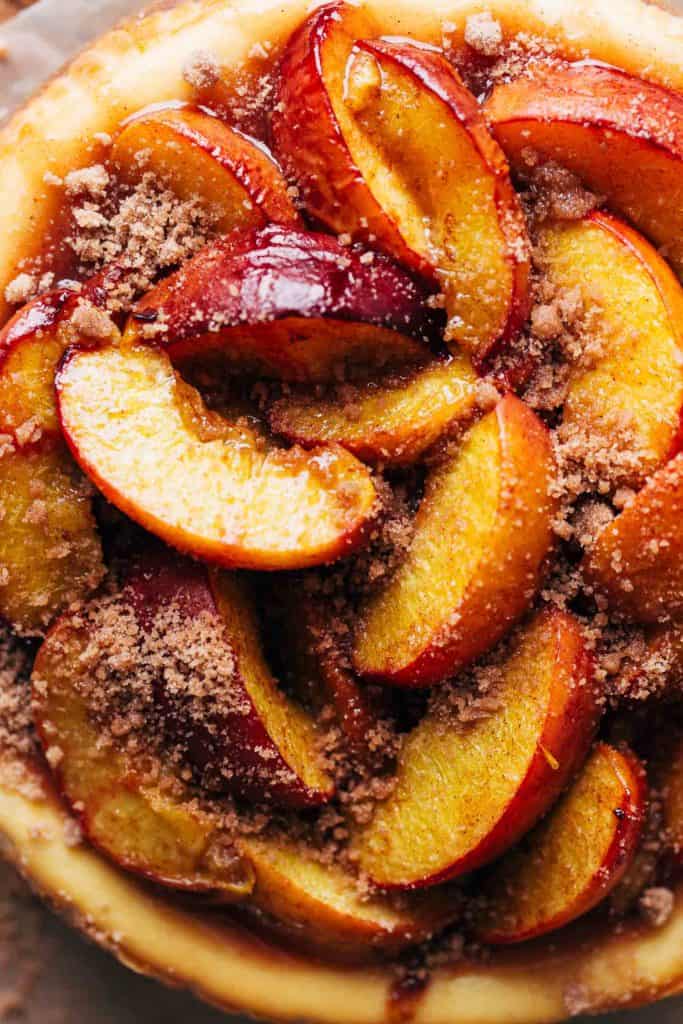 close up on the top of a peach cobbler cheesecake topped with a pile of roasted peaches
