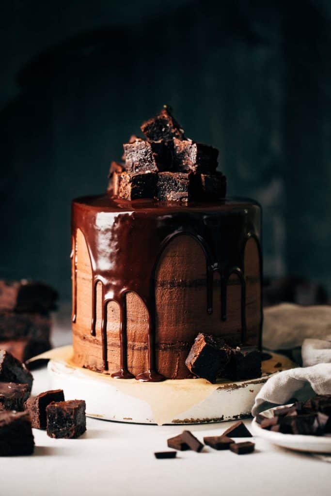 layered brownie cake covered in chocolate frosting, chocolate ganache drip, and a pile of brownies on top