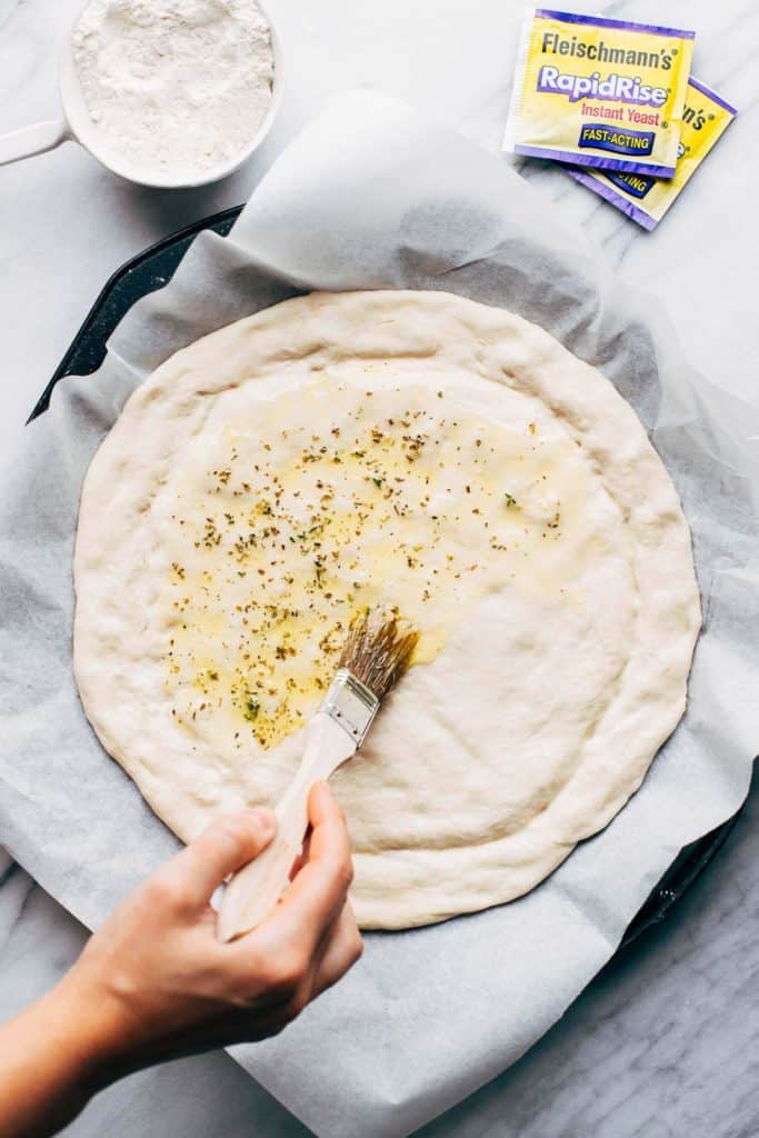 brushing pizza dough with oil and herbs