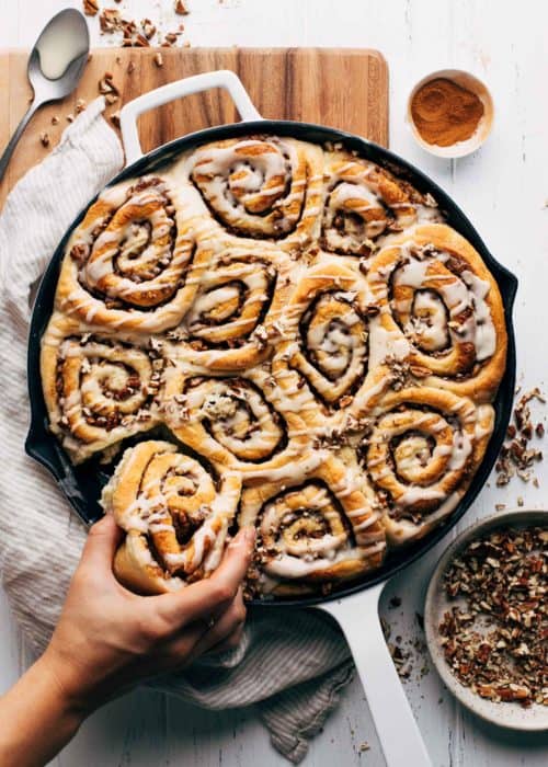 pulling a maple pecan cinnamon roll from the pan