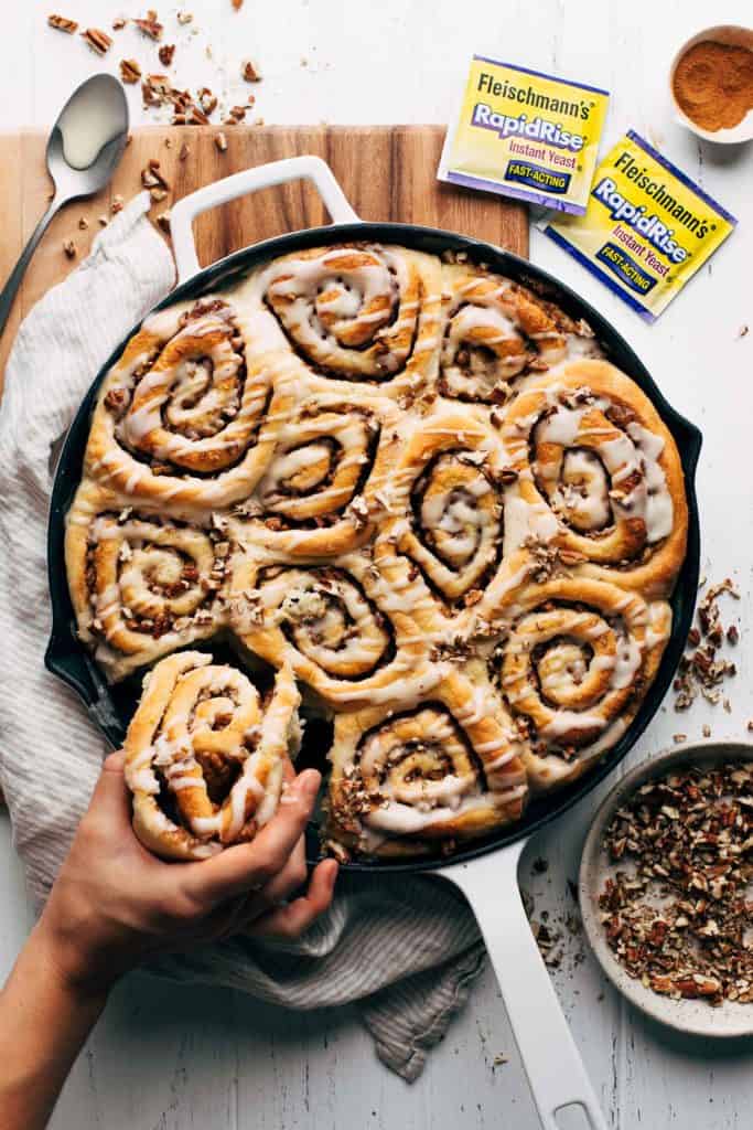 pulling a maple pecan cinnamon roll from the pan