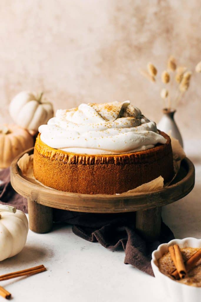 pumpkin cheesecake on a stand, topped with a pile of whipped cream