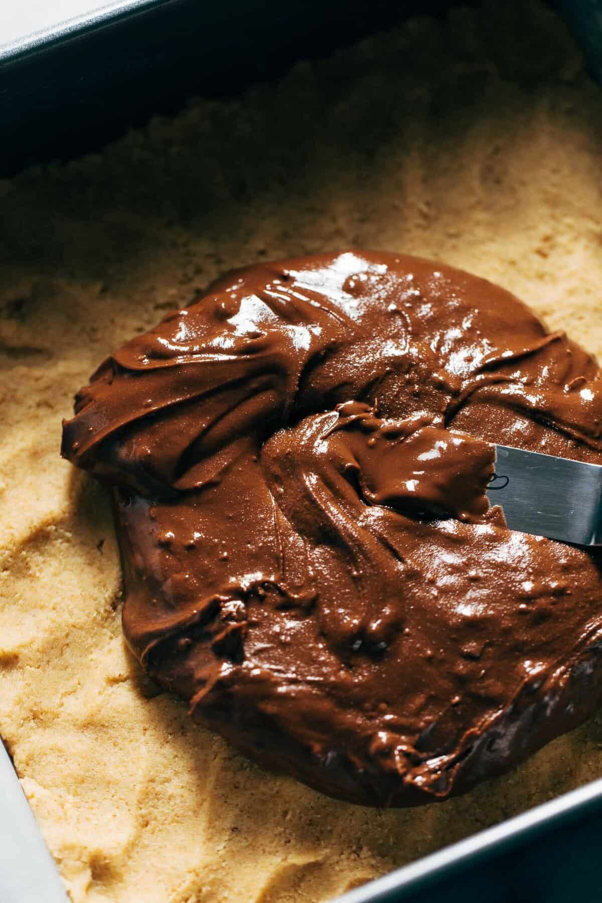 spreading chocolate sunbutter on top of a graham cracker cookie dough base