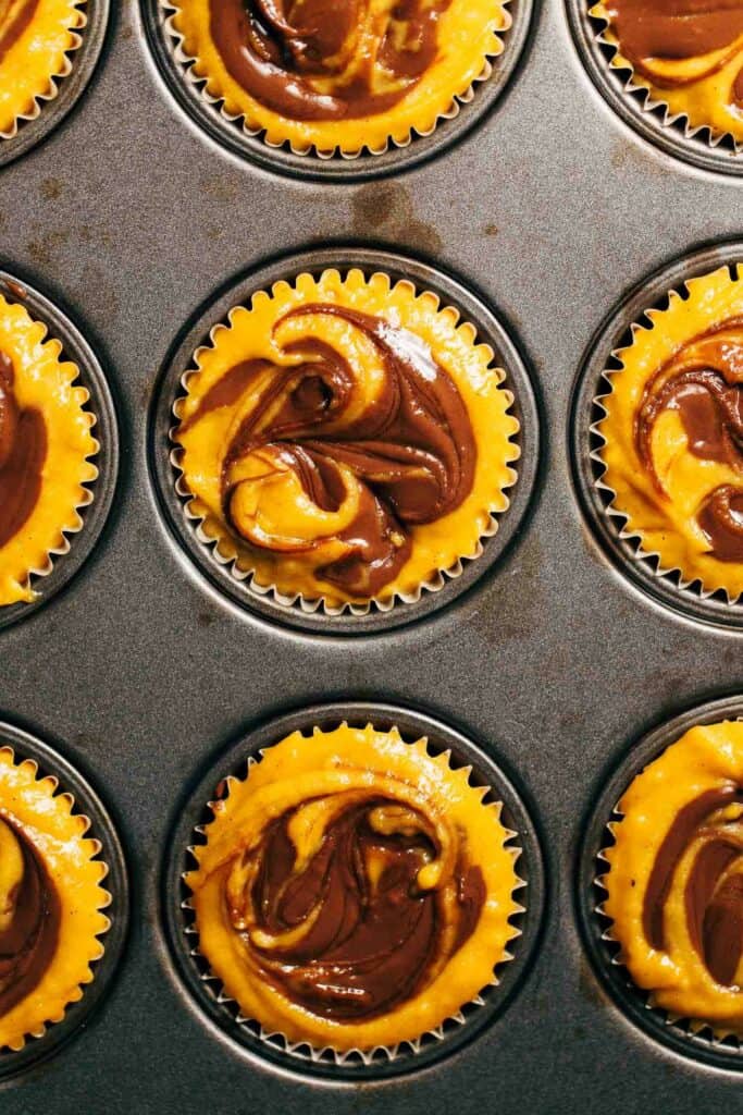 pumpkin muffin batter in a cupcake tin with chocolate swirls