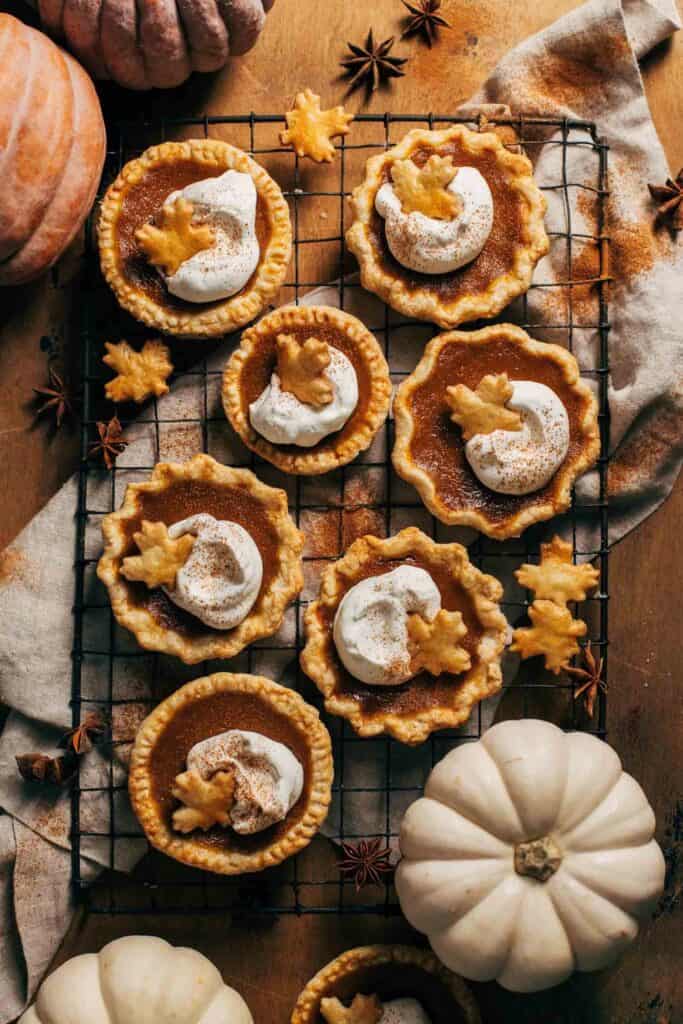 mini pumpkin pies topped with whipped cream and a pie crust maple leaf