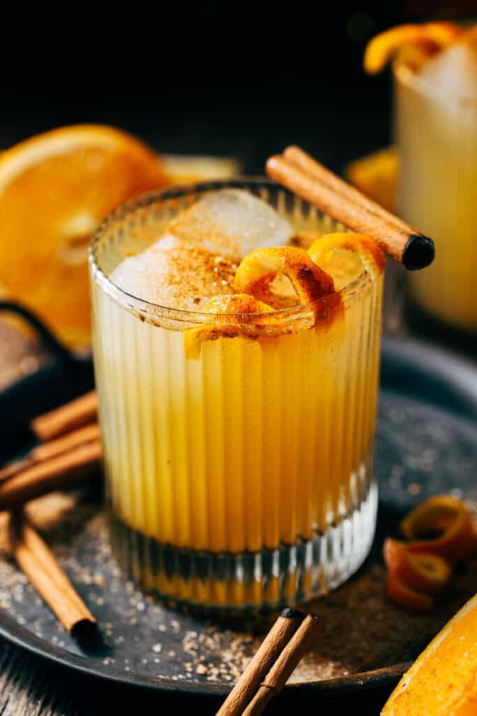 close up on an orange cocktail garnished with a cinnamon stick